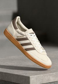 Sneaker bianca in suede con dettagli marroni, dotata di tre strisce, suola in gomma e branding "SPEZIAL" sul lato. Design con lacci.