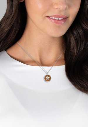 Silver chain necklace featuring a circular pendant with a wood inlay and a floral design embossed on a light brown background.