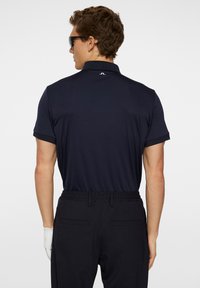 Marinblå kortärmad pikétröja med klassisk krage och kontrasterande detaljer, matchad med svarta byxor med elastisk midja och en vit handske.