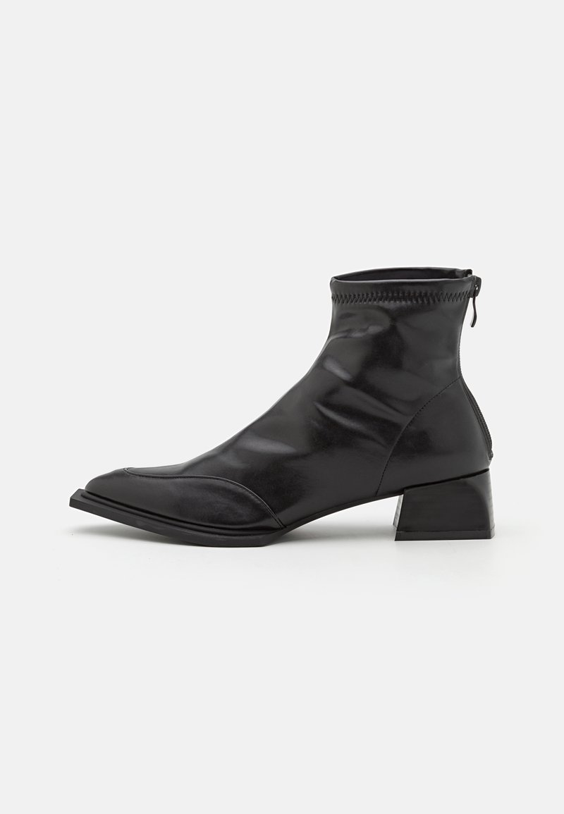 Bottines noires en matière synthétique brillante. Elles présentent une pointe effilée, un talon carré bas et une fermeture éclair à l'arrière.