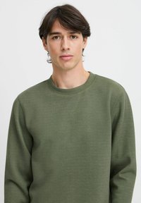 Sudadera de cuello redondo en verde oliva, fabricada en una mezcla de algodón, con mangas largas y una textura en la tela. Diseño simple con un corte holgado.