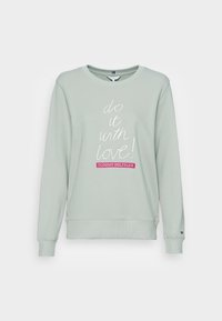 Sudadera de cuello redondo verde claro con el texto en cursiva blanca "¡hazlo con amor!" y parche del logo de Tommy Hilfiger en rosa centrado en la parte delantera.