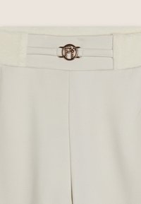 Pantaloni bianchi su misura con una fascia in vita testurizzata, caratterizzati da una fibbia circolare in metallo dorato con dettagli del logo e un tessuto elegante e liscio.