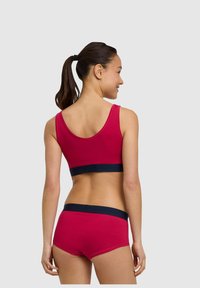 Czerwona bawełniana braletka z granatową opaską, zestawiona z pasującymi czerwonymi szortami z granatowym pasem. Gładka struktura, prosty design.