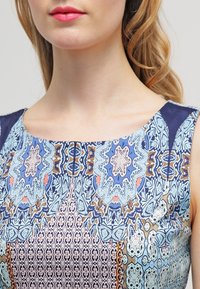 Šaty bez rukávů s jemnými modrými a růžovými geometrickými vzory, hladkým materiálem a kulatým výstřihem.