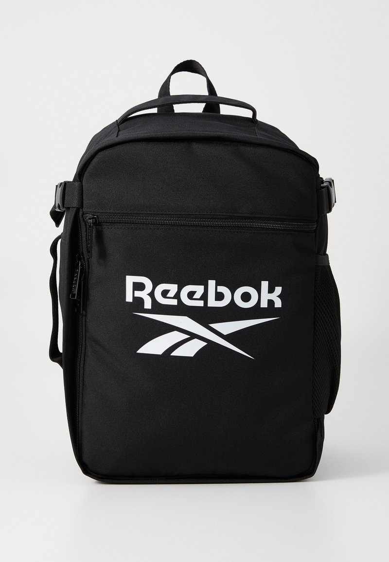 Črn Reebok nahrbtnik, izdelan iz trpežnega materiala, s prostornim žepom na zadrgo, ročajem na vrhu in izrazitim belim logotipom.