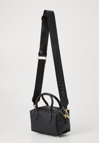 Črna usnjena torbica z teksturiranim zaključkom, z zlatimi dodatki, dvema zgornjima ročkama in snemljivim trakom, ki nosi vtisnjen logotip. Kompaktna zasnova.
