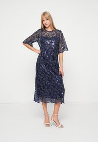 Robe à sequins navy avec un corsage ajusté et des manches courtes évasées, dotée d'un ourlet en dents de scie et de motifs en vagues complexes.