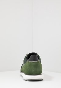 Sneaker verde in suede con accenti neri, suola bianca in contrasto e retro testurizzato. Design low-profile con tallone imbottito e forma slanciata.