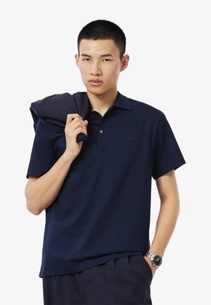Polo de color azul marino hecho de algodón, con una tapeta de dos botones y un logo bordado en el pecho. Textura suave, mangas cortas.