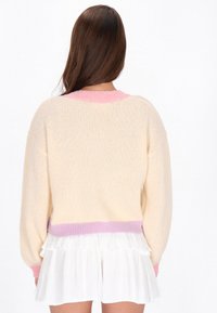 Sweter dziany o luźnym kroju, w kolorze kremowym, z różowymi akcentami na okrągłym dekolcie i brzegach, z prążkowanymi mankietami oraz miękką teksturą. Połączony z białą spódnicą z falbankami.