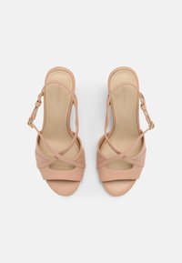 Nude high-heeled sandals with crisscross straps, open-toe design, smooth synthetic leather, and a secured ankle buckle.