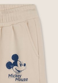 Pantaloni tuta beige con vita elasticizzata, presentano una stampa blu di Topolino e dettagli in strass sul design. Due tasche laterali.