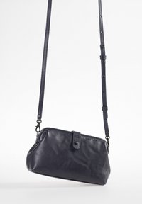 Navyfarbene Leder-Crossbody-Tasche mit weicher Textur, runder Form, verstellbarem Tragegurt und Druckknopfverschluss mit subtilen Logo-Details.