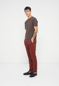 Camiseta marrón de manga corta combinada con pantalones slim-fit burdeos y zapatos negros tipo slip-on. El atuendo presenta un diseño simple y casual.