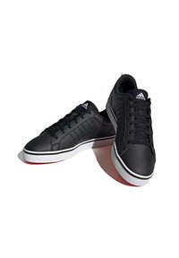 Zapatillas negras con una parte superior sintética suave, puntera redondeada y suela de goma blanca, acompañadas de cordones negros y un sutil detalle de rayas a los lados.