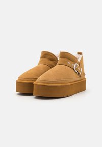 Zapatos de plataforma de ante en tono marrón claro con punta redondeada, un acento de hebilla en el costado y una suela texturada para mayor agarre y estabilidad.
