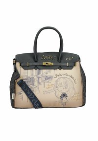Handtasche mit einem weichen beigen Körper, der schwarze Akzente, einen goldenen Verschluss und dekorative Kunstwerke mit einem stilisierten Mädchen und Text aufweist. Schwarzer Schultergurt ist enthalten.