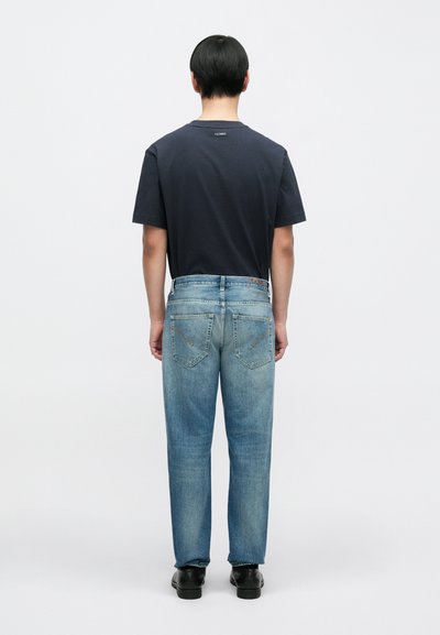 Jean en denim bleu clair avec un effet délavé, présentant une coupe droite et deux poches arrière. Associé à un T-shirt foncé.