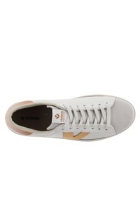 Zapatilla blanca de cuero con una puntera texturizada en gris y detalles en marrón claro, que presenta un logotipo prominente y cordones planos.