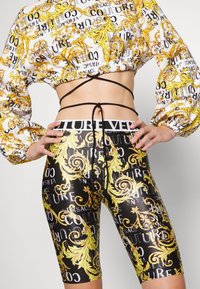 Haut court à manches longues et short cycliste taille haute avec motifs baroques noirs, blancs et dorés et texte répété "Versace Couture".