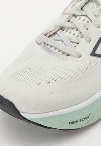 Bijela atletska tenisica s prozračnim teksturiranim gornjim dijelom, ravnim vezicama i svijetlozelenom pjenastom potplatom s oznakom "FRESH FOAM".