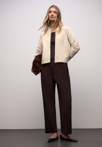 Prošívaná světle béžová bomber bunda se vzorem rybí kost, doplněná o tmavě hnědé široké kalhoty a černé špičaté baleríny.