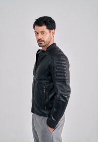 Czarna skórzana kurtka o dopasowanym kroju, z pikowanymi akcentami na ramionach, stójką oraz dwoma kieszeniami na suwak.