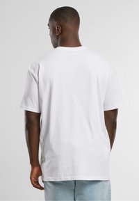 White cotton T-shirt with short sleeves, featuring a crew neckline and a relaxed fit, shown from the back against a plain background.