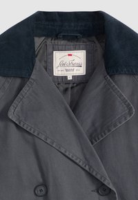 Grå dobbeltradet trenchcoat med en kordfløyelsnavykrage. Har fôr og et Levi Strauss-merke inni krageområdet.