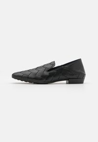 Scarpa slip-on in pelle intrecciata nera con punta affusolata e tacco basso, caratterizzata da una superficie testurizzata e dettagli di design minimi.