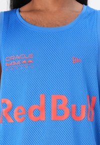 Modra mrežasta majica brez rokavov z napisom "Red Bull" v velikih rdečih črkah, z logotipom "Oracle Red Bull Racing" v manjšem tisku na levi strani.