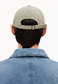 Casquette de baseball kaki avec sangle ajustable à l'arrière, portée avec une veste en denim bleue, montrant un tissu texturé et un design décontracté.