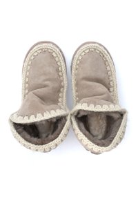 Zapatillas de gamuza marrón con diseño doblado, ribete trenzado crema, interior suave y forma de punta redonda. Sin herrajes visibles ni patrones.