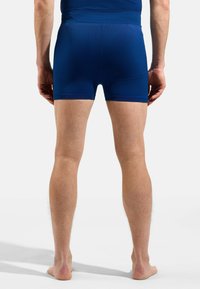 Blue athletic shorts made from stretchy fabric, featuring a textured waistband and leg openings, ending mid-thigh, worn barefoot.