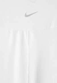 Biela tkanina zblízka s centrálnym švom a malým sivým logom Nike swoosh blízko hornej hrany.