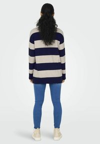 Gestreifter Pullover in Beige und Marineblau, mit langen Ärmeln, lockerer Passform, kombiniert mit blauen Skinny-Jeans und hellen Knöchelstiefeln.