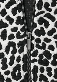 Tissu à imprimé léopard noir et blanc avec une fermeture éclair. La texture semble côtelée, avec des motifs noirs marqués sur un fond plus clair.