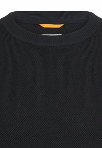 Ciemny dziany sweter z prążkowanym, okrągłym dekoltem, z kontrastującą pomarańczową metką z tyłu. Tekstura jest gładka i równomiernie wzorzysta.