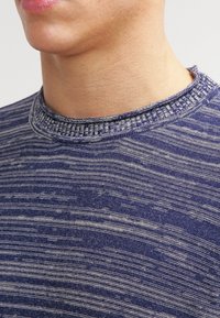 Tummansininen neule, jossa on teksturoidusta raidallisesta kuviosta ja ribbaus kaula-aukossa. Kangas näyttää pehmeältä, ja siinä on hienovaraisia värieroja.