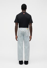 Μαύρο βαμβακερό μπλουζ άκι με στρογγυλή λαιμόκοψη και κόκκινο γραφικό στην πλάτη, συνδυασμένο με ανοιχτό μπλε, φαρδιά τζιν παντελόνια και μαύρα παπούτσια.