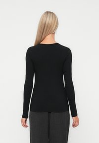 Top negru cu mânecă lungă, din material cu textură și croială ajustată, cu decolteu rotund, asortat cu pantaloni gri cu talie înaltă și croială largă.