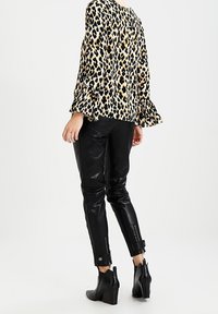 Blouse à imprimé léopard avec des manches à volants, associée à un pantalon skinny noir brillant avec des fermetures éclair aux poignets et des bottines à talons.