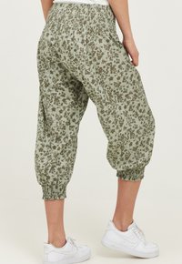 Lysegrønne bukser med blomsterprint, elastisk talje og manchetter; lavet af blød, struktureret stof; parret med hvide sneakers.