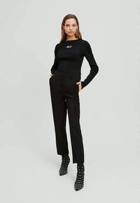 Melnas krāsas garām piedurknēm tops ar izšūtu logotipu, sapārots ar melnām augsta vidukļa biksēm un melniem potīšu zābakiem ar plankumiem. Gluda tekstūra, pieguļošs dizains.