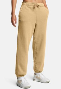 Beige bomullssvettisar med elastisk midja och justerbar dragsko; ribbade muddar, sidofickor, minimal logotyp på låret.