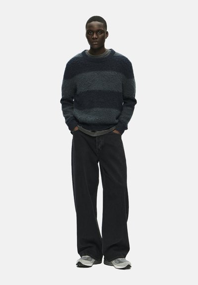 Gebreide trui met horizontale donkerblauwe en grijze strepen, gecombineerd met losse zwarte jeans en grijze sneakers; gedetailleerde textuur van de stof.