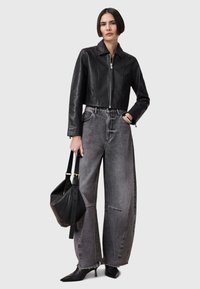 Chaqueta de cuero negro cortada con cremallera frontal, combinada con jeans de mezclilla grises holgados con dobladillo con flecos. Bolso negro y tacones puntiagudos.