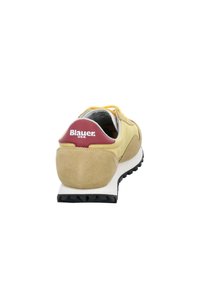 Sneaker gialla e beige con suola nera e linguetta rossa etichettata "Blauer USA," mostrata da dietro su uno sfondo bianco.