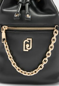 Zwarte leren emmer tas met een gouden kettingaccent, een gladde textuur, een ritsvak en een merklogo aan de voorkant.